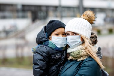 Şehirdeki sokakta maskeli çocukların olduğu bir aile. Anne ve çocuk koronavirüs ve grip salgını sırasında yüz maskesi takıyor. Virüs ve hastalık koruması, kalabalık yerlerde el dezenfektanı..