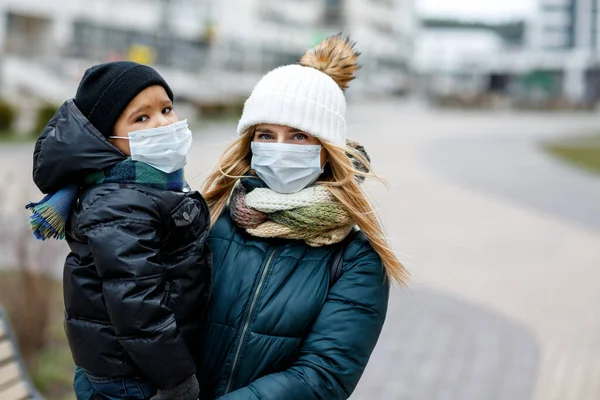 Şehirdeki sokakta maskeli çocukların olduğu bir aile. Anne ve çocuk koronavirüs ve grip salgını sırasında yüz maskesi takıyor. Virüs ve hastalık koruması, kalabalık yerlerde el dezenfektanı..