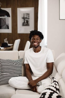 Genç bir Afro-Amerikalı Konmat 'ta kanepede oturuyor ve gülümsüyor. Güzel bir erkek gülüşü. 