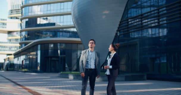 Twee collega 's kletsen op straat tijdens de lunchpauze in de buurt van het gebouw op de achtergrond. Ze staan in een moderne straat vol met glazen gebouwen en structuren. Communicatie van collega 's — Stockvideo