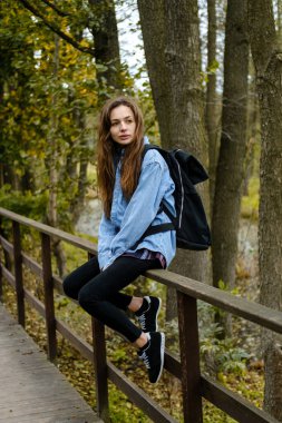 Sırt çantalı bir kadın turist sonbahar ormanında bir köprüde oturuyor..