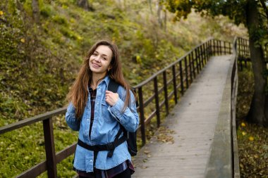 Sırt çantalı bir kadın turist sonbahar ormanında bir köprüde yürüyor..