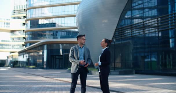 Twee collega 's kletsen op straat tijdens de lunchpauze in de buurt van het gebouw op de achtergrond. Ze staan in een moderne straat vol met glazen gebouwen en structuren. Communicatie van collega 's — Stockvideo