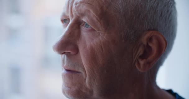 Een close-up portret van een bejaarde man van in de 60, die uit het raam kijkt Gedachten over ouderdom — Stockvideo