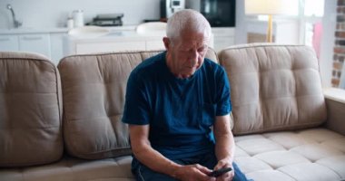 Çocuklar için bir mesaj. Yaşlı bir adam kanepeye oturur ve üzgün bir şekilde cep telefonuna bir mesaj yazar. Bir adamın portresi..