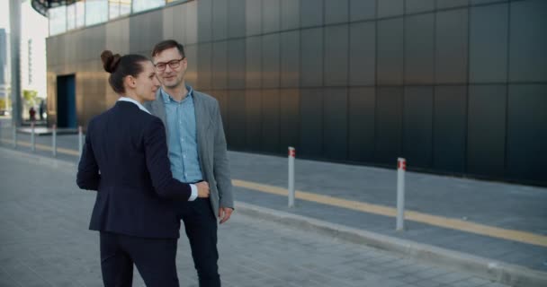Twee managers, een man en een vrouw, ontmoeten elkaar op straat tegen de achtergrond van een modern gebouw en bespreken een businessplan tijdens een wandeling door de stad. Werkplannen voor de week. Werkbesprekingen. — Stockvideo
