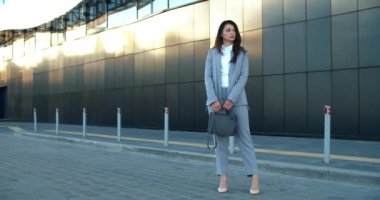 İş kıyafetleri içinde genç ve güzel bir kadın camdan evleri olan modern bir caddede duruyor. Kadın, iş arkadaşını bekliyor. İş konsepti.