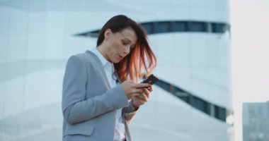 İş stili olan güzel bir kadın sokakta duruyor ve telefonda bir mesaj yazıyor. Kapıcı kadın, yakın plan..