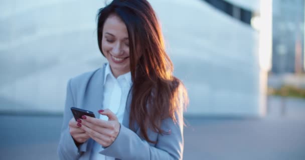 Een mooie vrouw in een zakelijke stijl staat op straat en schrijft een bericht aan de telefoon. Vrouwelijke portier close-up. — Stockvideo