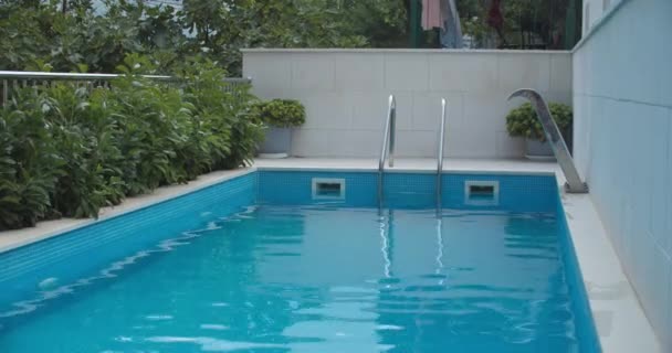 Piscina all'aperto con vista sulle piante verdi. Acqua limpida riempie la piscina. Pulire l'acqua chiara da vicino — Video Stock