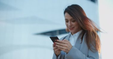 İş stili olan güzel bir kadın sokakta duruyor ve telefonda bir mesaj yazıyor. Kadın portresi..