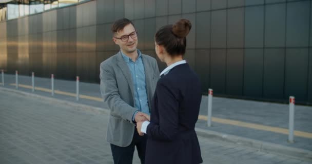 Alegre sonriente joven pareja de colegas de negocios se reúnen cerca del centro de negocios en la calle, saludar y hablar sobre temas de trabajo. Comunicación de colegas en la calle. — Vídeo de stock