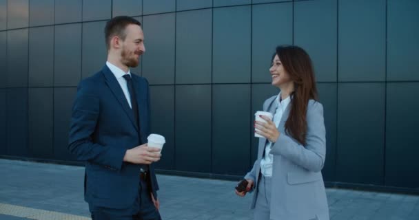 Alegre sonriente joven pareja de colegas de negocios se reúnen cerca del centro de negocios en la calle, beber café y charlar. Comunicación de colegas en la calle. Retrato de una mujer y un hombre — Vídeo de stock