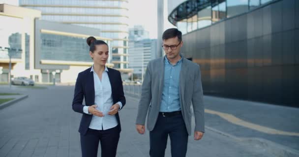 仕事の同僚の男性とビジネススタイルの女性は、近代的な建物の近くに行き、仕事のトピックを議論しています。同僚のコミュニケーション. — ストック動画