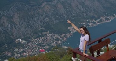 Güzel gülüşlü mutlu kadın dağın tepesinde duruyor ve iki parmağını gösteriyor. Özgürlük sembolü.