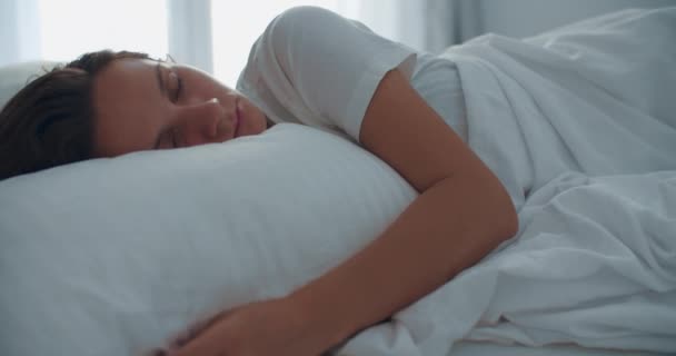 Šťastná žena, která se ráno probudí po spánku, leží v posteli. Světlá ložnice. Detailní záběr portrét ženy — Stock video