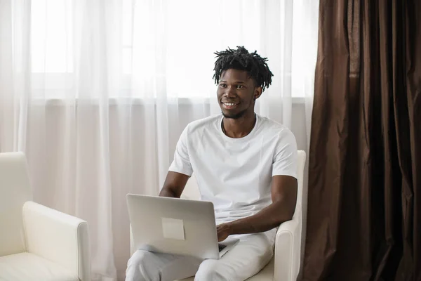 Happy african american man with dreadlocks, enjoying watching educational webinar on laptop. Smiling young mixed race businessman holding video call with clients partners.