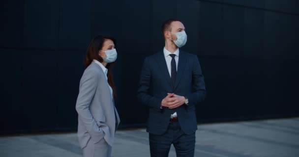 I colleghi in giacca e cravatta e maschere protettive si trovano vicino a un edificio moderno e parlano di argomenti di lavoro. Ritratto femminile e maschile — Video Stock