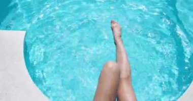 İnce bacaklar havuzda berrak mavi suya yakın çekim yapıyor. Bir kadın bacaklarını suda hızla hareket ettirir, damlalar farklı yönlere uçar.