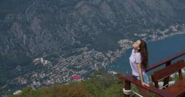 Genç mutlu kadın dağın tepesinde duruyor ve güzel bir manzaraya bakıyor. Eller yukarı!.