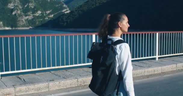 Glückliche Touristinnen mit schwarzem Rucksack gehen die Autobrücke entlang. Blick auf die blaue Bucht und die Berge — Stockvideo