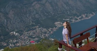 Genç mutlu kadın dağın tepesinde duruyor ve güzel bir manzaraya bakıyor. Eller yukarı!.