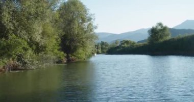 Bir grup turist bir yaz akşamı nehirde bir tekneyle açılıyorlar. Yeşillik ve dağ manzarası. Tekne gezisi