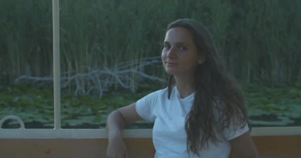 Gelukkige vrouw met krullend haar drijft op een boot op de rivier. Haar haar blaast in de wind. De vrouw geniet van de rit. Vrouwelijk portret — Stockvideo