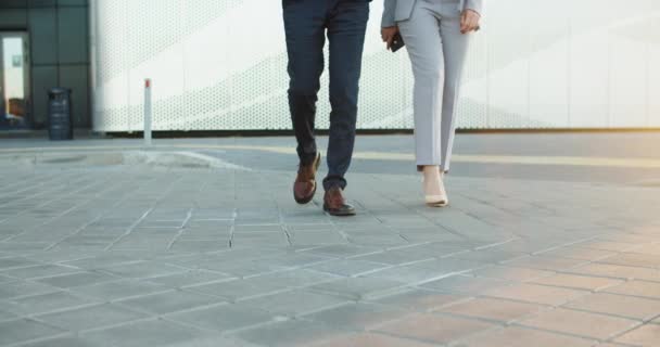 Primer plano de pies femeninos y masculinos. Los colegas de negocios están caminando cerca de un edificio completamente nuevo durante un descanso de trabajo. Luz del atardecer — Vídeos de Stock