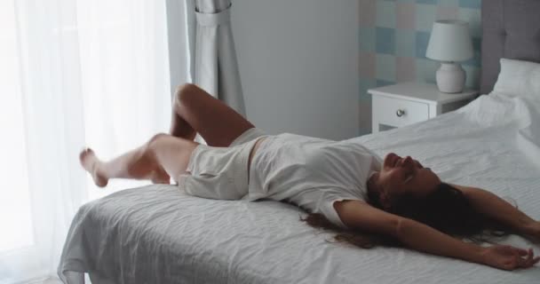 Šťastná brunetka se ráno probudí, cvičí a skočí na postel. Šťastná žena. — Stock video