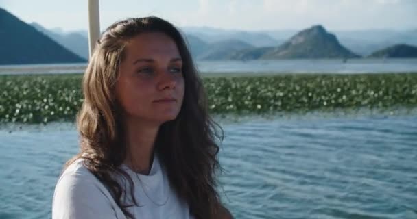 Μια νεαρή μελαχρινή γυναίκα πλέει σε μια βάρκα σε μια όμορφη λίμνη και εξετάζει τη φύση. Γυναίκα αχθοφόρος κοντά — Αρχείο Βίντεο
