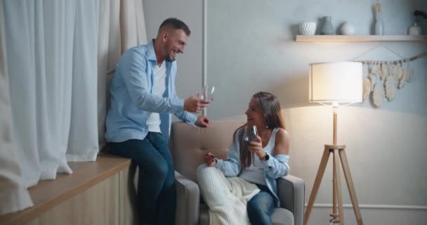 El marido y la esposa celebran unas vacaciones en familia, beben vino en casa en un sillón. Pareja risa y alejarse — Vídeos de Stock