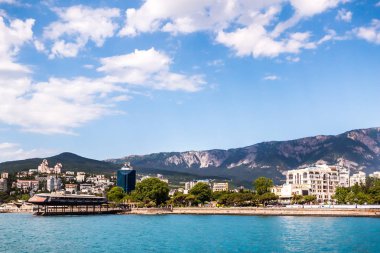 Görkemli dağ sırtı yakınındaki sakin deniz kıyısında yer alan modern turistik şehir manzarası