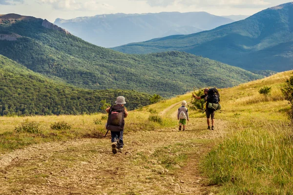 Anonim üst ve sırt çantaları güneşli günde engebeli arazi seyahat ederken kırsal yolda yürürken iki çocuk