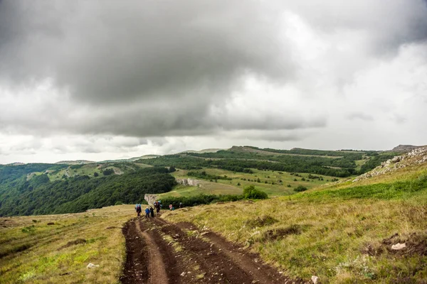 Unrecognizable people walking on countryside road on grassy slope of hill on beautiful cloudy day in wonderful nature