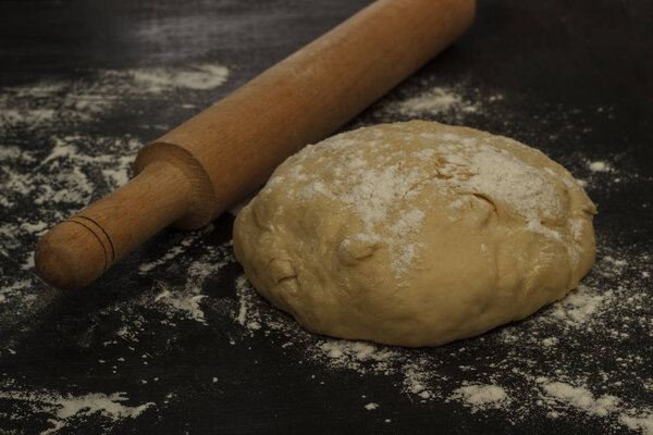 round dough and rolling pin on a dark background