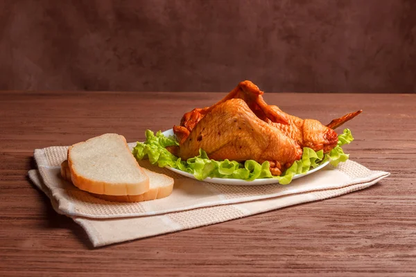 Smoked chicken wings with bread and lettuce in a white plate on a napkin