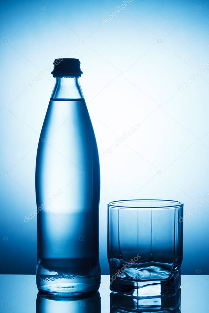 Bottle of water and empty glass on blue background