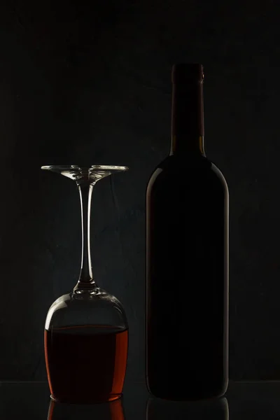 Flaska och glas med vin på en mörk bakgrund i motljus — Stockfoto