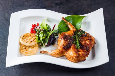 Bıldırcın tütün beyaz bir plaka üzerinde ızgara. Yeşiller, soğan ve rasmarin ile