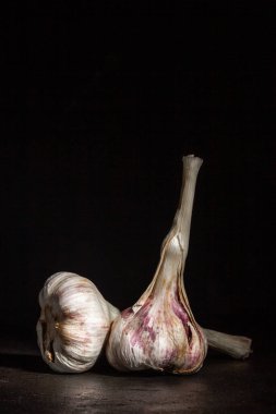 İki baş sarımsak, koyu bir arka plana karşı.
