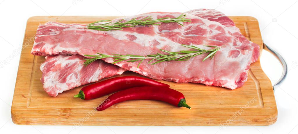 Raw pork ribs on a board with rosemary, garlic, hot pepper and tomatoes