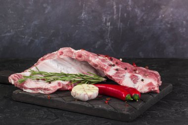 Koyu bir tahtada çiğ domuz pirzolası, biberiye, acı biber ve şiş.