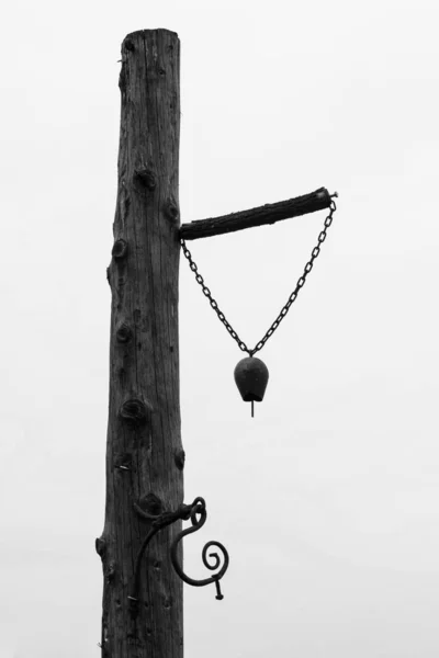 Una vieja campana utilizada en la granja montada sobre un pilar de árbol de madera - Blanco y negro — Foto de Stock