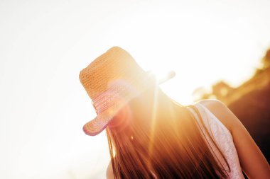İyi günler tamamlama. Şapkalı bir kız günbatımında görünüyor. Sıcak yaz gecesi. Kız ve güneş ışınlarının.
