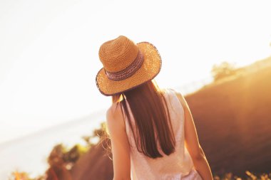 Şapkalı bir kız günbatımında görünüyor. Sıcak yaz gecesi. Kız ve güneş ışınlarının