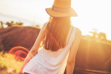 Şapkalı bir kız günbatımında görünüyor. Sıcak yaz gecesi. Kız ve güneş ışınlarının