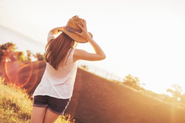 Kız şapka tutan ve gün batımında görünüyor. Sıcak yaz gecesi. Kız ve güneş ışınlarının