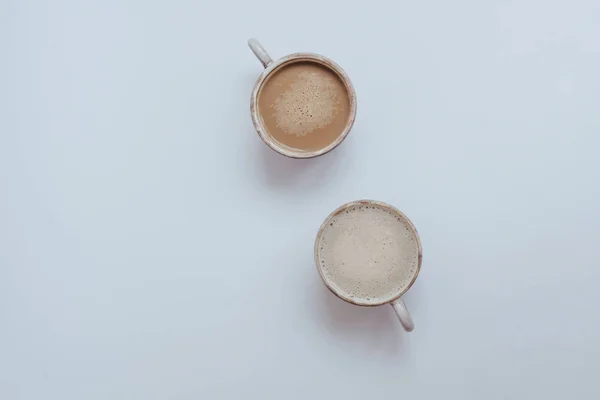 Two cups of fragrant coffee on a white table, top view