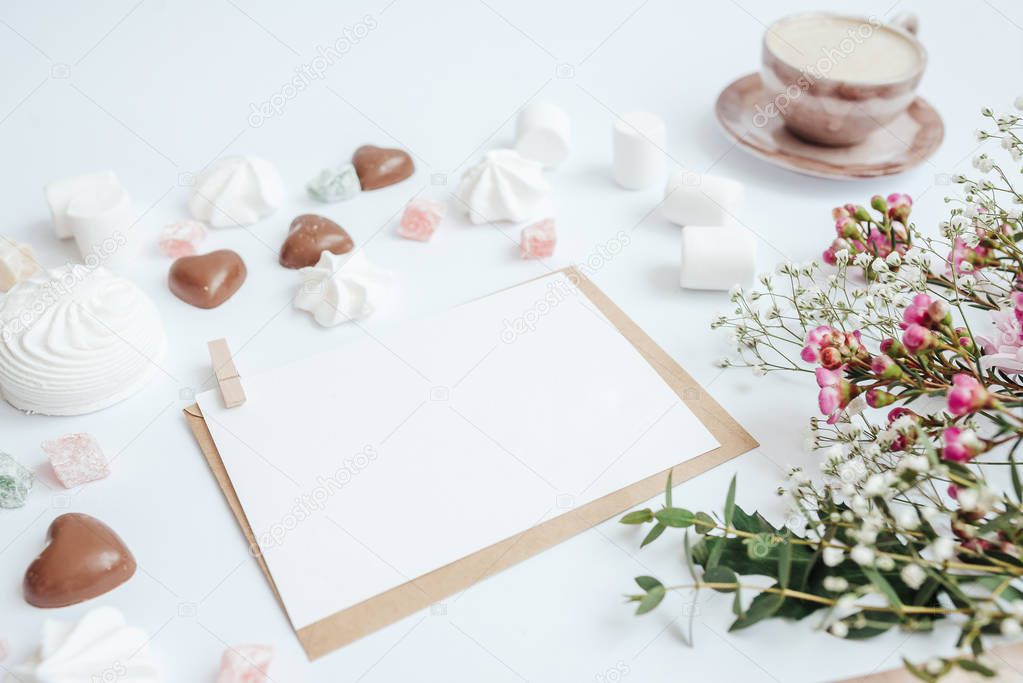 White card on a craft envelope. Coffee, sweets and flowers on a white background